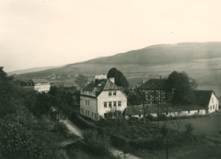 Das Fachwerksgebäude rechts ist die alte Mühle; Neubauten sind in der Mitte das sog. Lehrgebäude und hinten links das sog. Akademiegebäude; dahinter sind die ersten Häuser von Adelshausen zu erkennen; im Vordergrund die Landstraße.Foto nach 1922 und vor 1926.